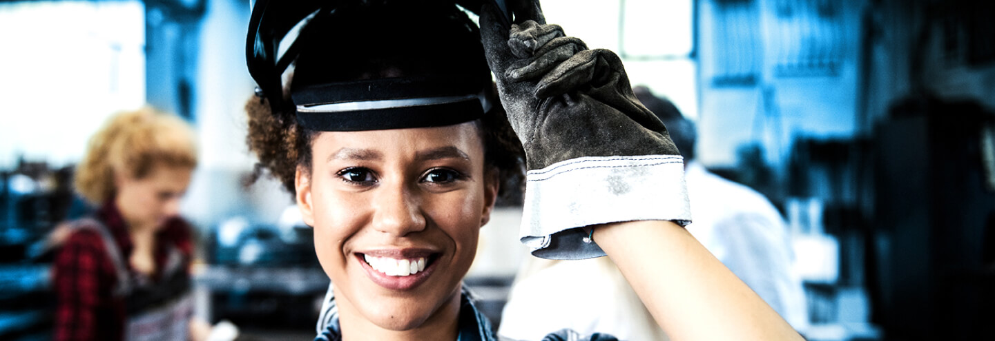Frau, die lächelt und einen Schweißer-Helm auf Ihrem Kopf trägt.